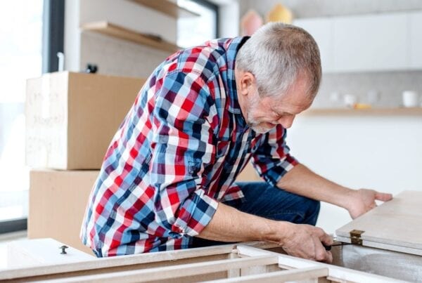 A grey-haired man fixes kitchen cupboards ready to be fitted