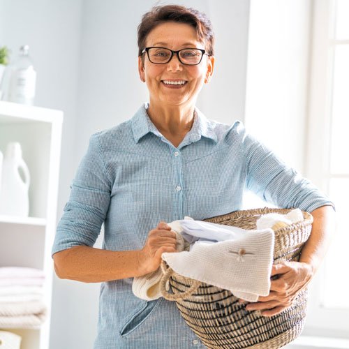 A middle-aged woman smiles holding a basket of clean laundry