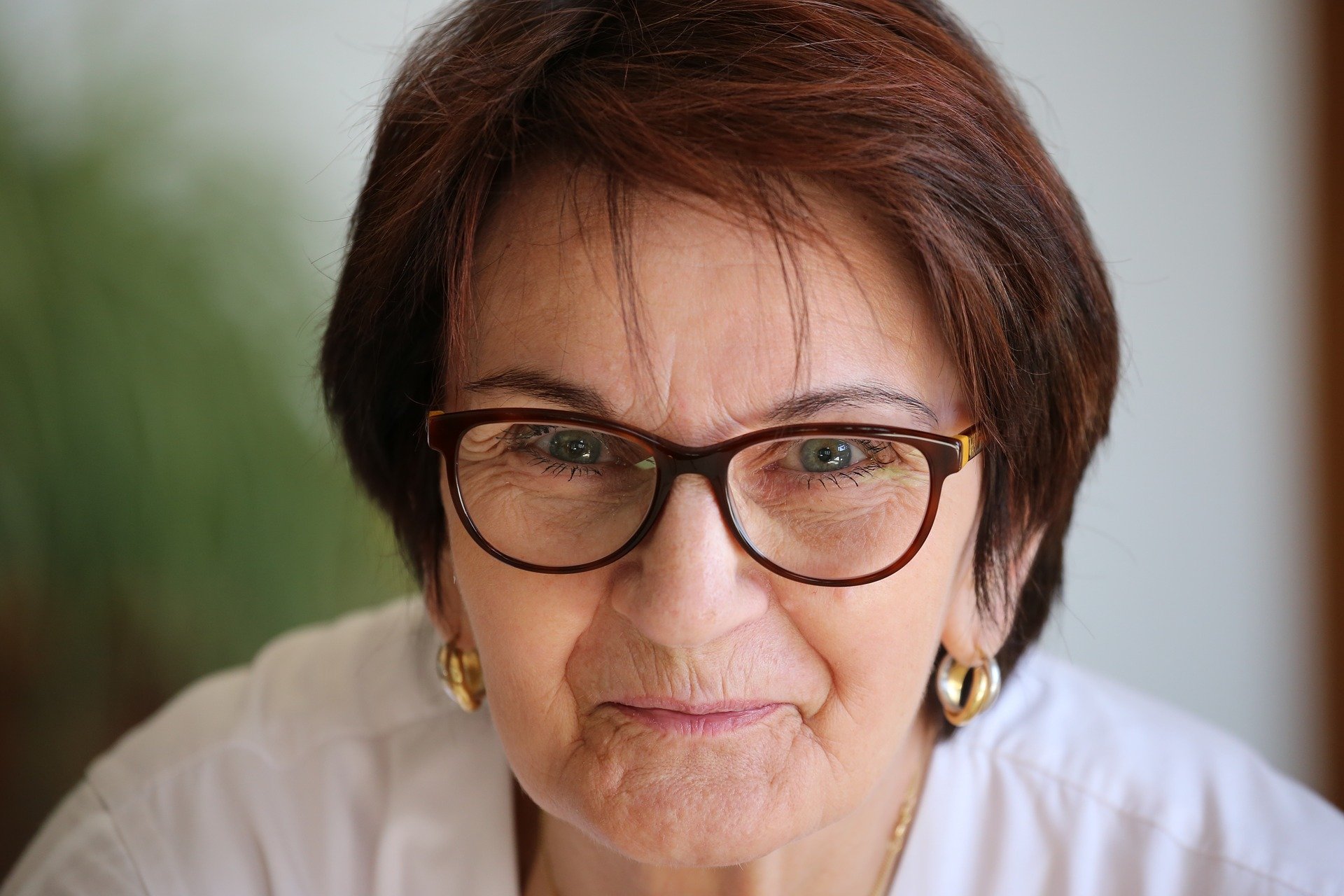 A smiling older lady with short red hair and red glasses