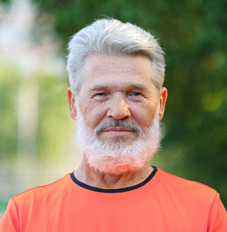 A grey-haired man in an orange top lifting weights